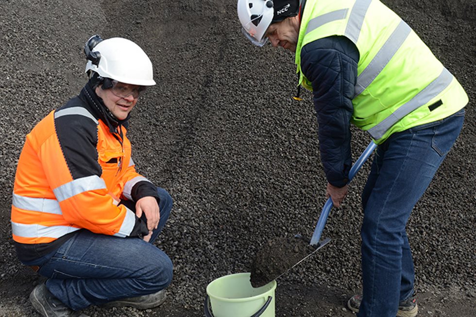 Man kneeled next to a bucket where another person is shoveling aggregate to. 