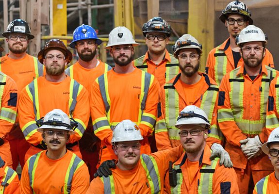 Group of men in orange protective jumpsuits posing in front of a grinding mill