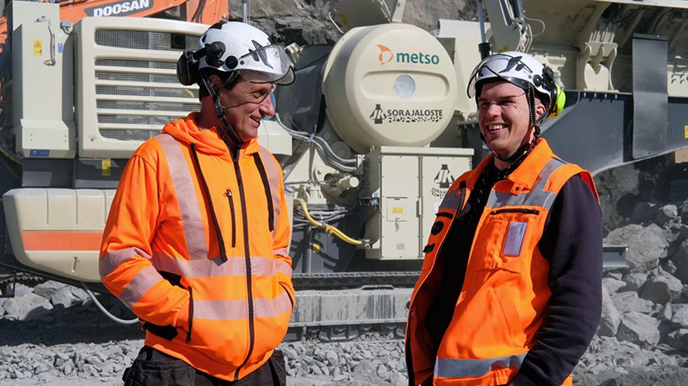 Kaksi miestä juttelemassa louhoksella, taustalla Lokotrack.