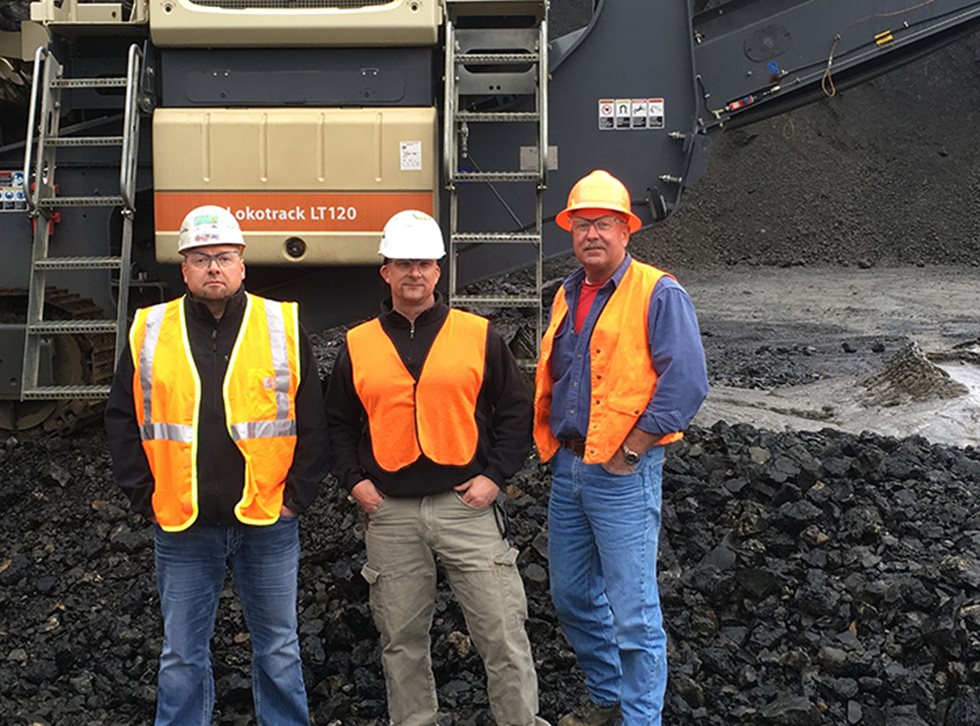 Three people posing in front of Lokotrack LT120.
