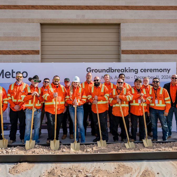A group of people dressed in orange PPE holding shovels and standing in front of a backdrop at Metso's ground breaking ceremony