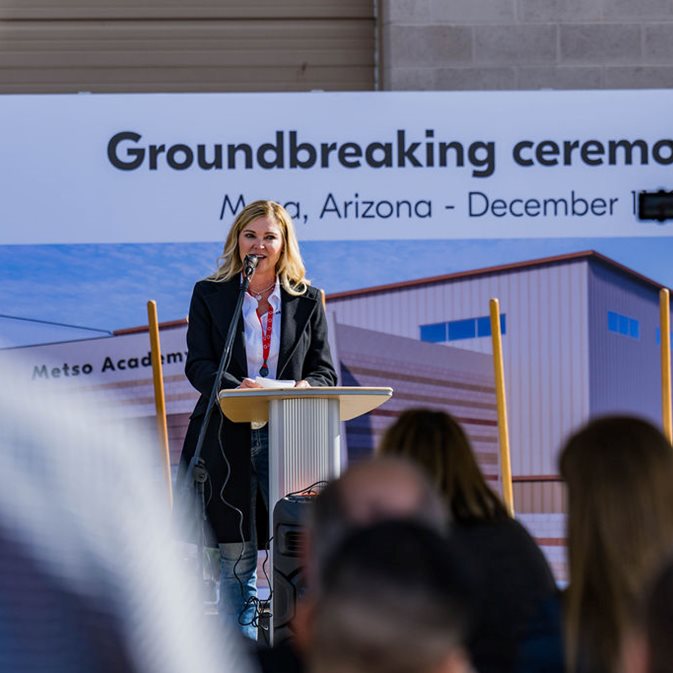 Woman standing in front of a backdrop, speaking into a microphone to a crowd of people at Metso's groundbreaking ceremony