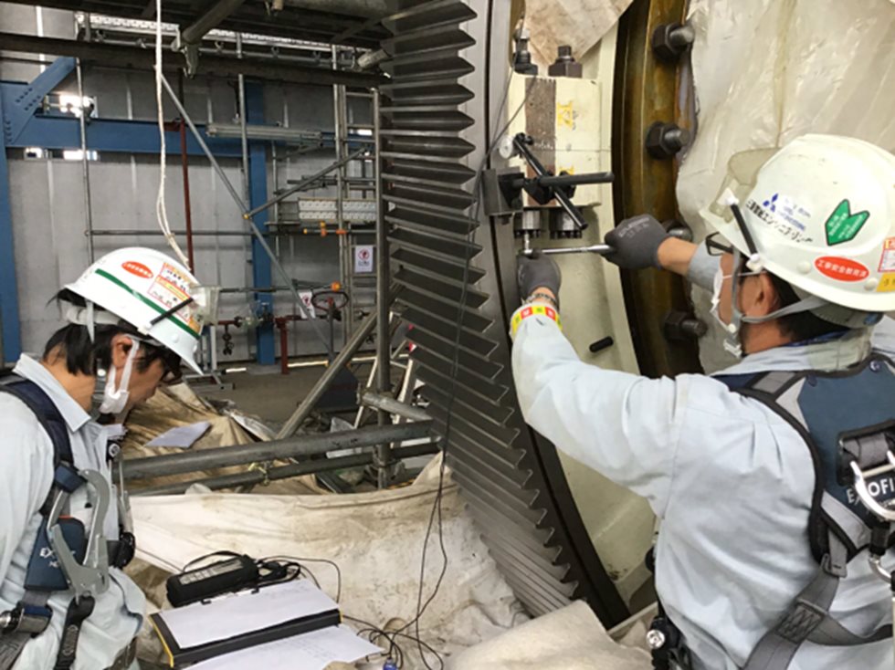 Two men working around a grinding mill gear.