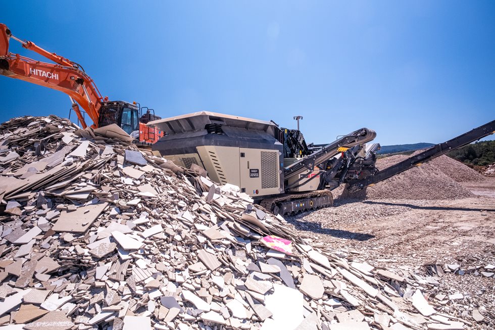 El triturador de impacto móvil Metso Nordtrack I908S con pantalla integrada está triturando y cribando eficazmente el excedente de residuos de azulejos cerámicos para ser reutilizados en el proceso de fabricación de azulejos.